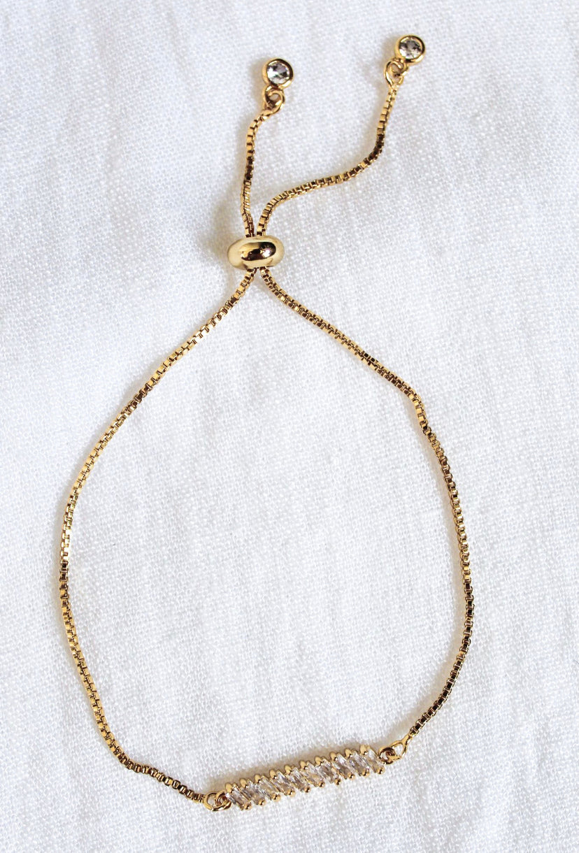 The Dupre Adjustable Bracelet by Kinsey Designs Archives features a 14k gold filled chain, a cubic zirconia-studded bar, and an adjustable sliding clasp, elegantly displayed on white fabric.