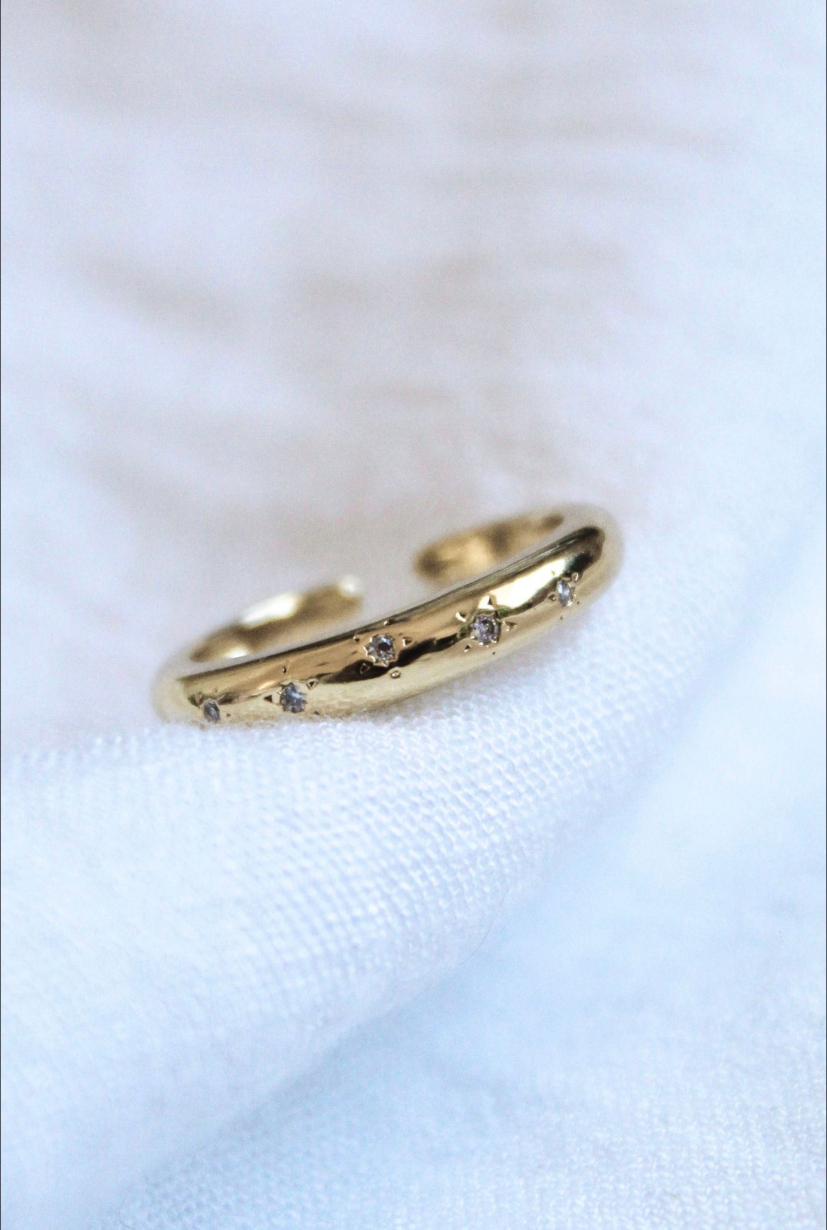 The Gia Ring by Kinsey Designs Archives, gold plated and size 7 with small embedded diamonds, rests on a soft white fabric background.