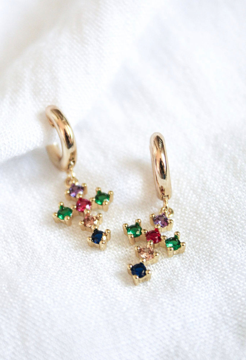 The Tori Huggie - Clear by Kinsey Designs Archives features gold filled hoops with dangling clear cubic zirconia crosses, displayed on a white fabric background.