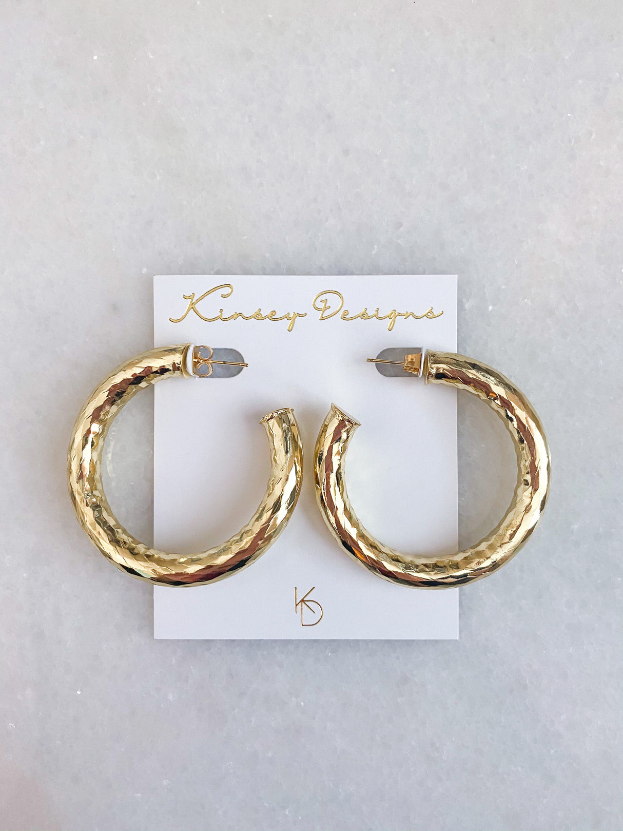 The Jasmine Hoops by Kinsey Designs are gold filled hammered hoop earrings, shown on a white Kinsey Designs card against a marble background—perfect for statement jewelry lovers.