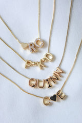 The Charm Bar Necklace Box Chain - Kinsey Charm Bar features gold-filled, adjustable necklaces with letter pendants displaying "RO," "PKD," "QUINN," and "COE" on a white background, combining elegance and durability.