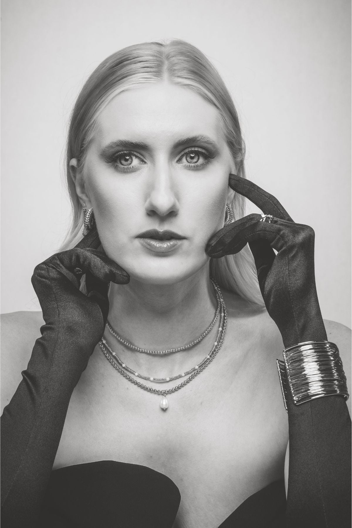 Black and white photo of a woman with long hair wearing black gloves, layered necklaces, and a strapless top.