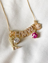 The Kinsey Charm Bar Necklace Box Chain features charming and delightful gold-filled "HMM" charms, including a shoe, a clear gem, a pink heart, and a paw print set against a soft white fabric background. Fully adjustable for the perfect fit.