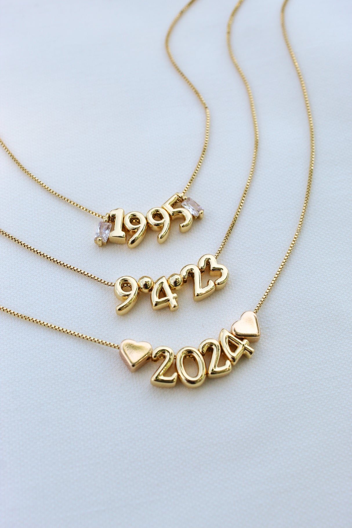 Four Numerical Slide - Kinsey Charm Bar gold-filled necklaces, featuring charm numbers '1995', '9423', '2024' and heart charms, beautifully arranged on a light background, perfect for adding elegance to your look.