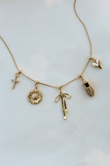 Gold-filled necklace with various charms including a cross, a sunflower, a bow, a pineapple, and the Vintage Heart Drop Charm from Kinsey Charm Bar on a plain white background.