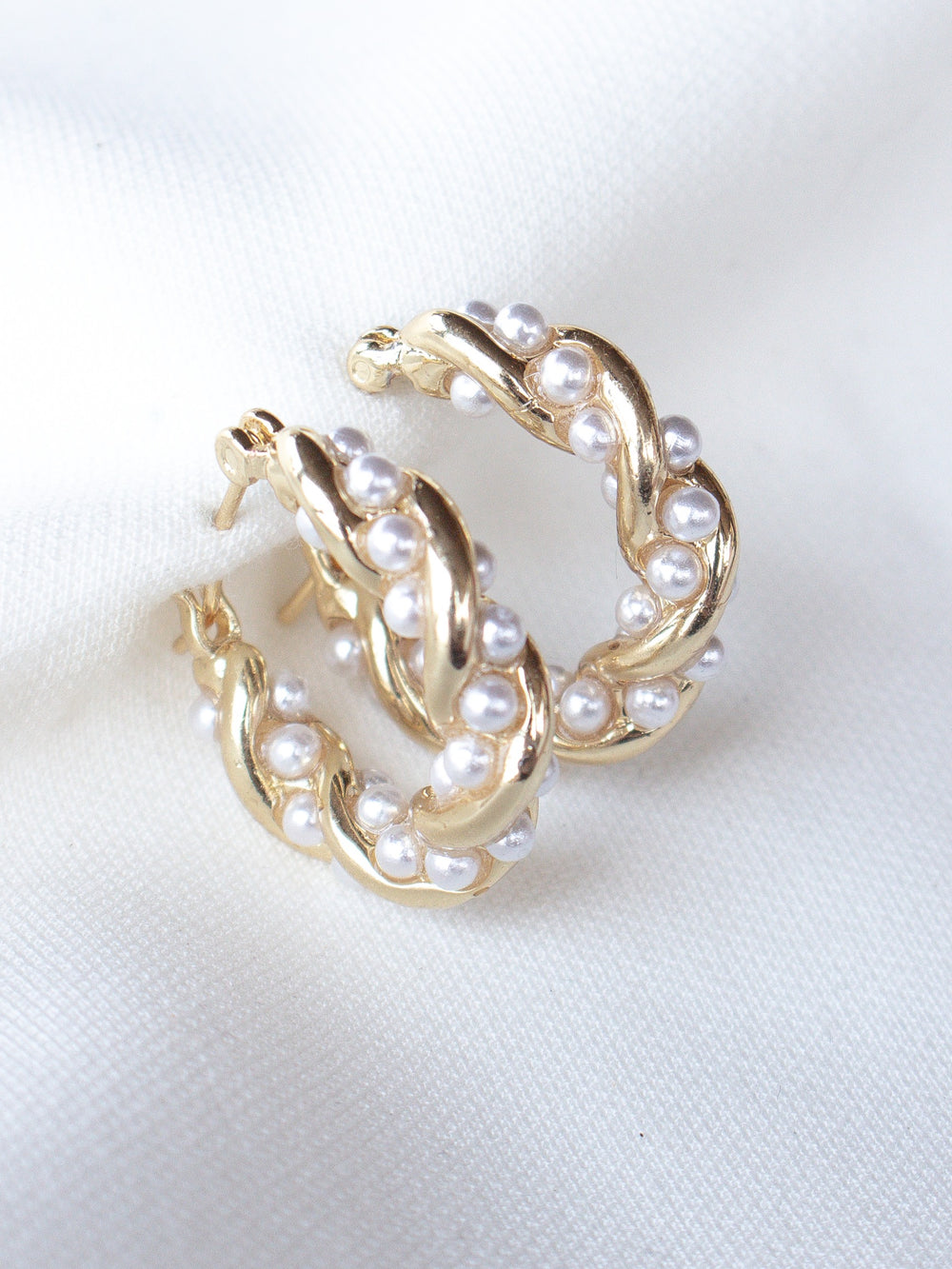 Audrey Pearl Hoops by Kinsey Designs: Gold hoop earrings with a twisted design, accented with small white pearls and shown on a white fabric background.