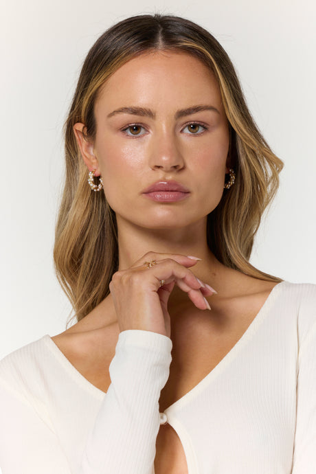 A woman with long blonde hair and a white top wears Kinsey Designs’ Audrey Pearl Hoops, gazing directly at the camera.