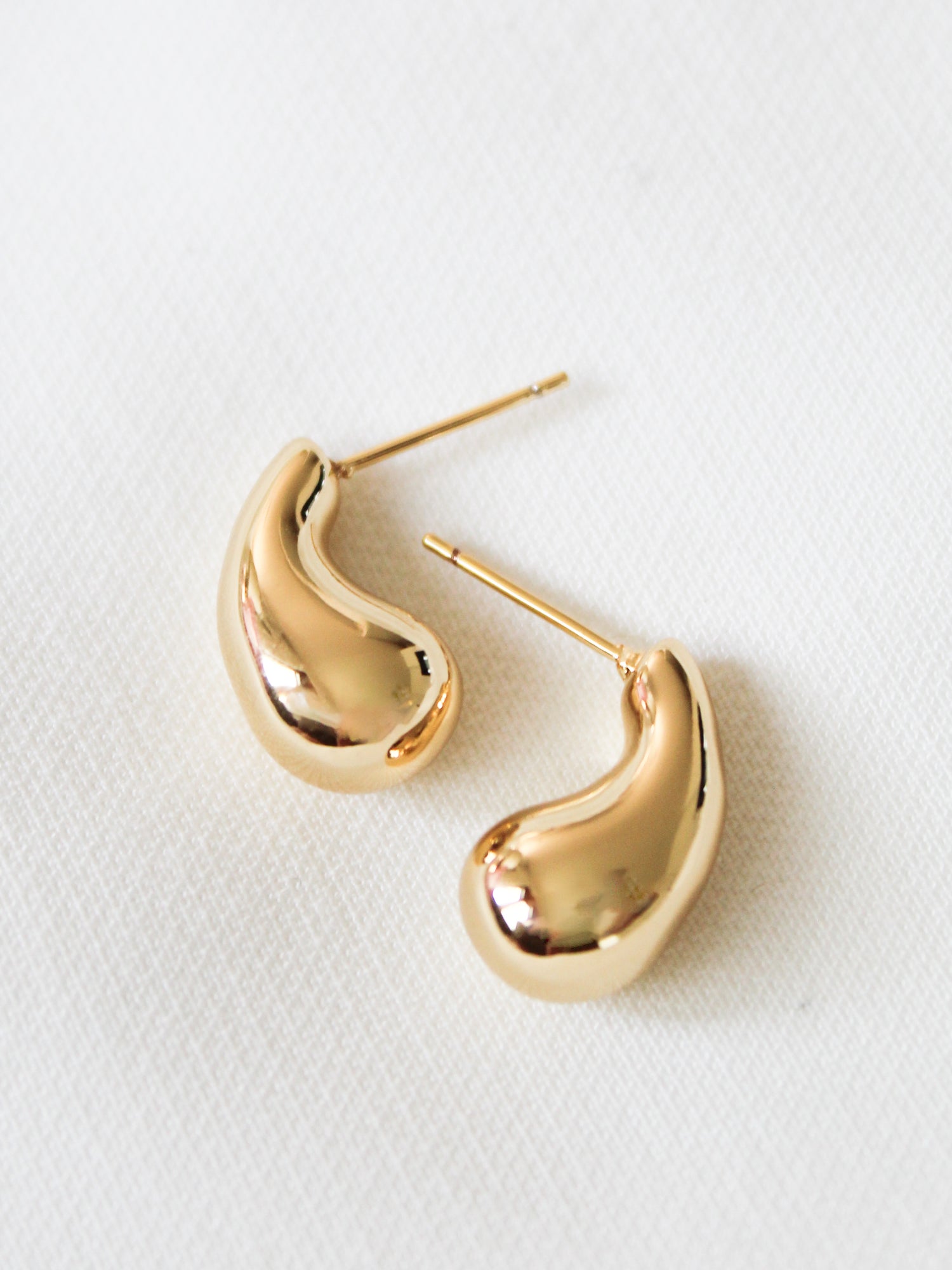 The Baby Drop Post by Kinsey Designs is a pair of gold filled, bean-shaped stud earrings measuring .75" long, shown on a white textured surface.