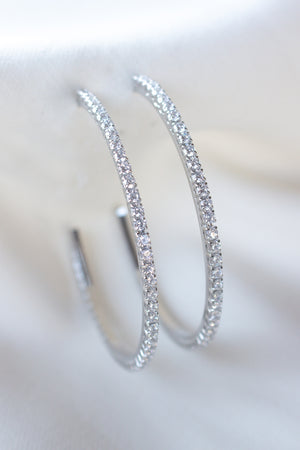 Close-up of Kinsey Designs’ Blaze Hoop Silver earrings, crafted from rhodium-plated brass and adorned with sparkling stones, displayed on white fabric.