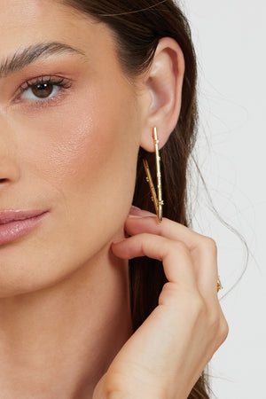 A woman with natural makeup touches her hair in a close-up while wearing Kinsey Designs' Bowen Earring Luxe gold-filled hoops.