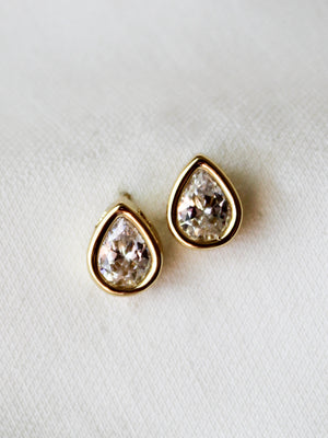 The Bridget Stud Earrings by Kinsey Designs feature teardrop-shaped clear gemstones set in gold, elegantly displayed on a white fabric background—an enduringly stylish piece for your jewelry collection.