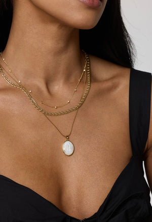 A woman wears the Kinsey Designs Pippa Necklace, a delicate gold-filled piece, layered with a pearl necklace and styled with a black dress, drawing attention to her neck and collarbone.