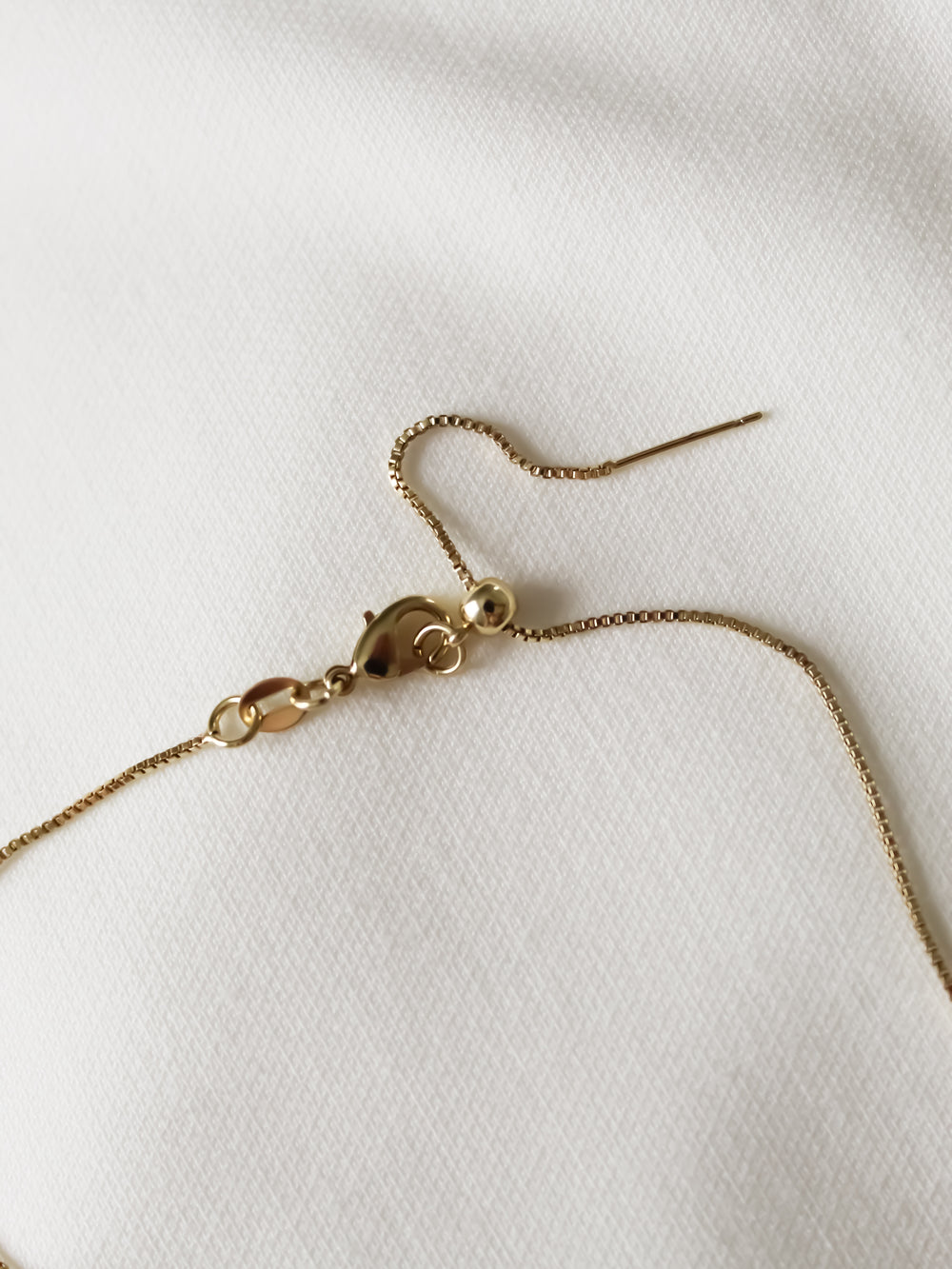 A delicate Charm Bar Necklace Box Chain - Kinsey Charm Bar, set on a white fabric background, featuring a lobster clasp and an adjustable extension chain.