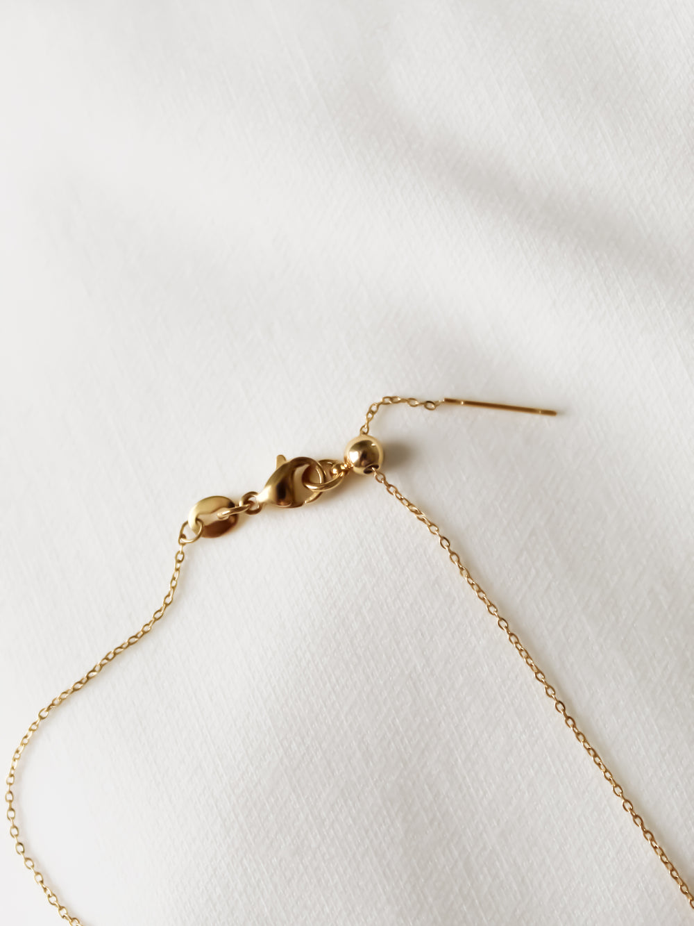 The NEW! Charm Bar Necklace Dainty Cable Chain – Kinsey Charm Bar, gold-filled with a delicate chain and clasp, lies gracefully on a white textured fabric.