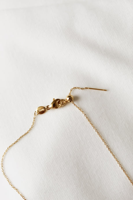 The NEW! Charm Bar Necklace Dainty Cable Chain – Kinsey Charm Bar, gold-filled with a delicate chain and clasp, lies gracefully on a white textured fabric.