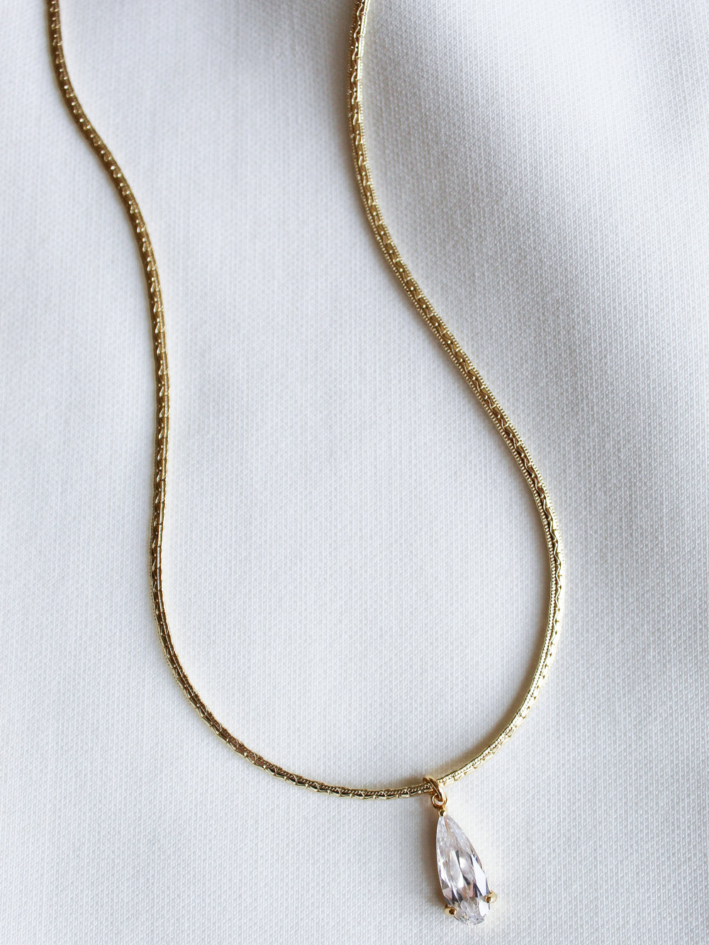 The Charlotte Drop Necklace by Kinsey Designs showcases a sparkling cubic zirconia teardrop pendant, elegantly displayed against a white fabric background.