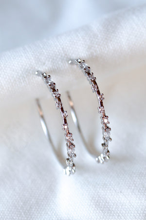 The Chase Hoop Large earrings by Kinsey Designs are silver hoops embellished with sparkling cubic zirconia, shown on a white fabric background.