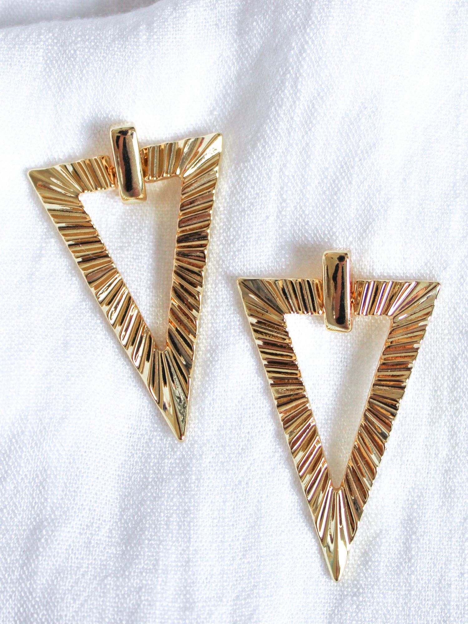 The Colin Earring by Kinsey Designs, featuring a gold textured triangular design, is showcased on a white fabric background.