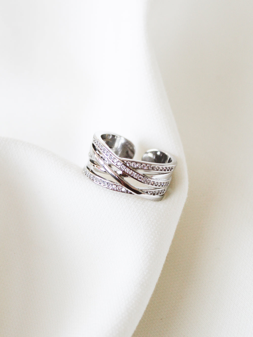 The Cris Ring by Kinsey Designs features stacked silver bands with small diamonds, displayed on white fabric—an elegant choice for an anniversary gift.