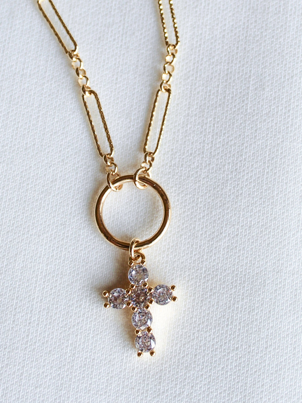 The Denise Necklace by Kinsey Designs features a gold-filled chain and a circular pendant with a crystal-studded cross, shown on a white textured background—an elegant choice for a baptism gift.