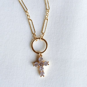 The Denise Necklace by Kinsey Designs features a gold-filled chain and a circular pendant with a crystal-studded cross, shown on a white textured background—an elegant choice for a baptism gift.