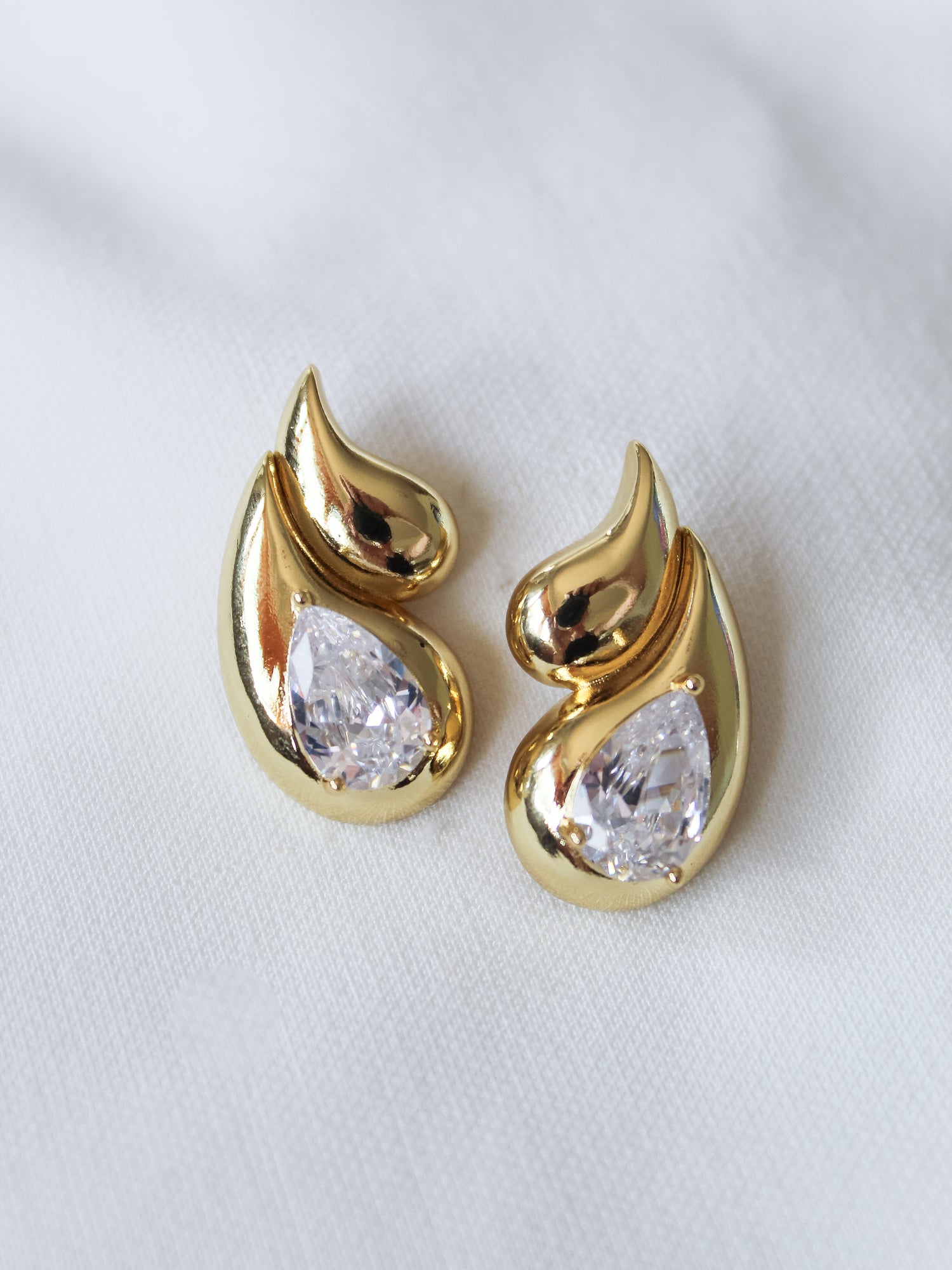 The Double Drop Stud by Kinsey Designs Archives features gold-filled teardrop shapes with clear gemstones, displayed on a white fabric background—an elegant addition to any jewelry collection.