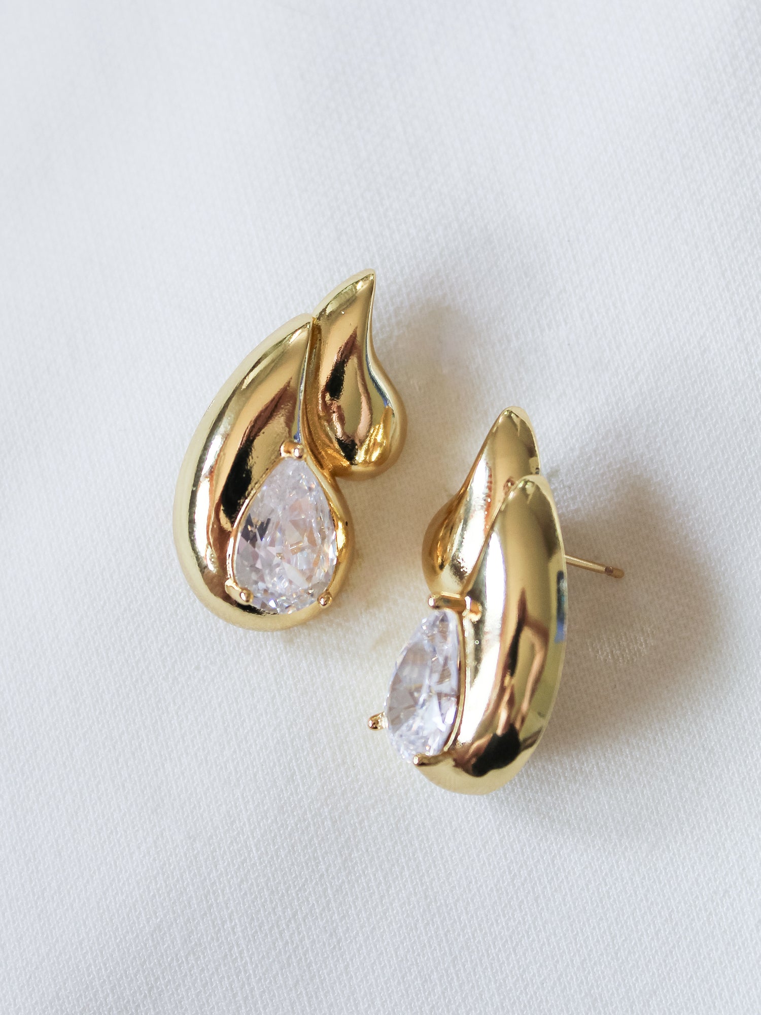 The Double Drop Stud by Kinsey Designs Archives features gold-filled teardrop earrings with clear gemstones, showcased on a white fabric background—ideal for elevating your jewelry collection or discovering a special piece at a sample sale.