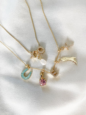 Charm Necklace Dainty Chain by Kinsey Designs Archives features five gold necklaces with unique pendants—horse, horseshoe, pearl, pink gem, and initials—on dainty chains for a personalized and stylish look.
