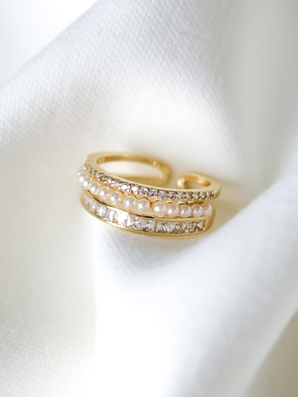 The Ellana Pearl Ring by Kinsey Designs features gleaming rows of pearls and diamonds on a crystal pavé band, showcased on soft white fabric.