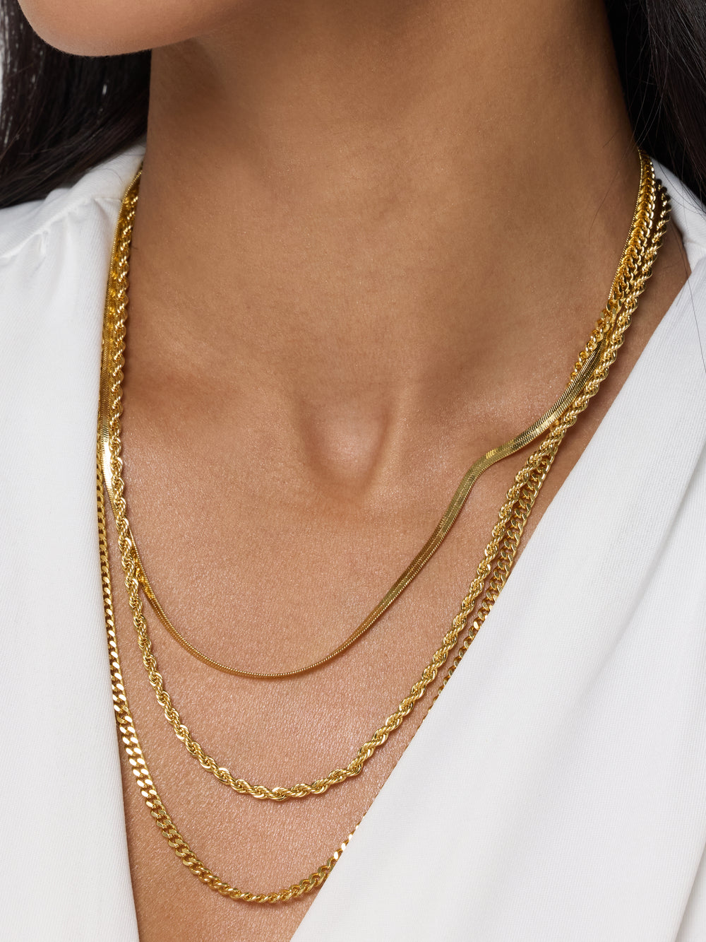 A woman wears a white top and the Emile Layer Necklace by Kinsey Designs Archives, a stunning multi-chain necklace that draws elegant focus to her neck and chest.
