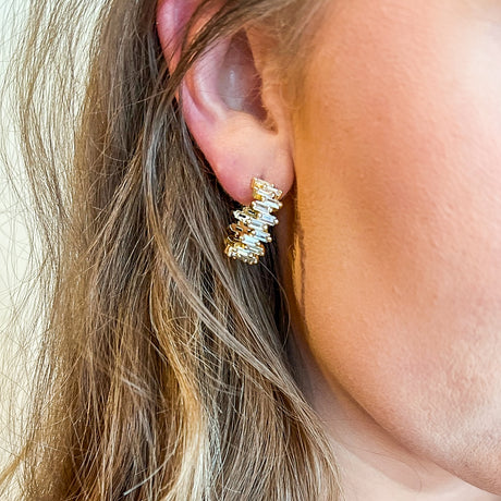 A close-up of a woman's ear wearing the Ettie Hoop by Kinsey Designs Archives, a 1" gold filled hoop earring featuring rectangular clear cubic zirconia gemstones.
