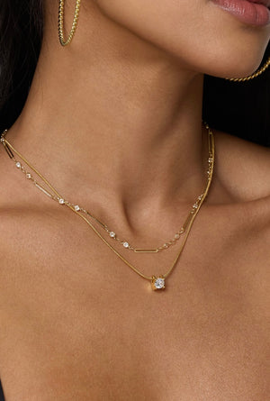 A woman models the Jenna Necklace by Kinsey Designs Archives—an 18-inch gold filled chain with gemstones—layered and paired with gold hoop earrings, shown from shoulders to chin.