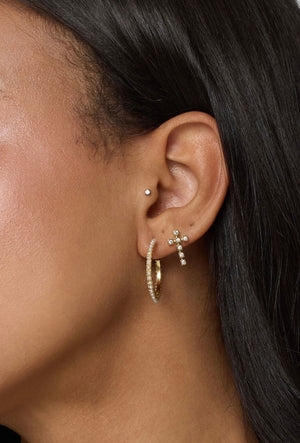Close-up of an ear wearing three earrings: a stud, a gold cross with small cubic zirconia stones, and the Kinsey Designs Archives Whit Hoop.