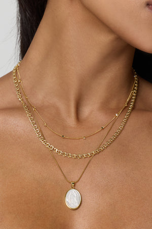 A woman wears the Kinsey Designs Archives Gabi Necklace, a three-layered gold filled set featuring an 18-inch chain with a round pendant, against bare skin.