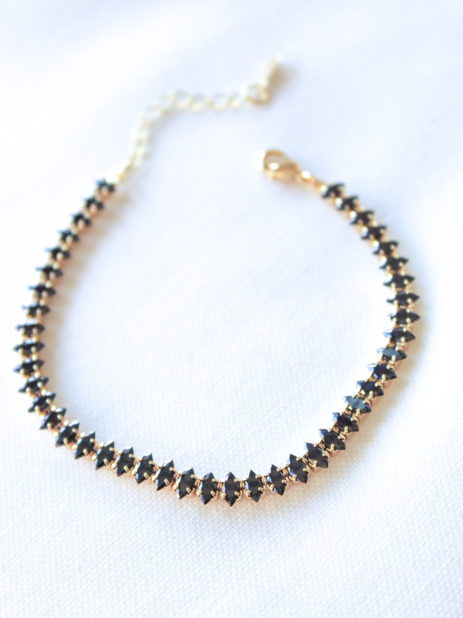 The Gator Mini Bracelet-Charcoal by Kinsey Designs Archives features gold plating and charcoal stones in a row, shown on white fabric. This item is part of our final sale.