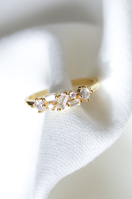 The Gavey Ring by Kinsey Designs Archives features small clear gemstones and is shown on a white textured fabric. Adjustable and perfect for stacking, this exclusive piece is available in our sample sale.