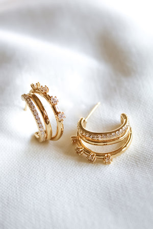 The Hallie Earrings by Kinsey Designs are gold-filled hoops, .75" in diameter, featuring sparkling stones and floral accents—ideal for elevating your jewelry collection. Displayed on a white fabric background.