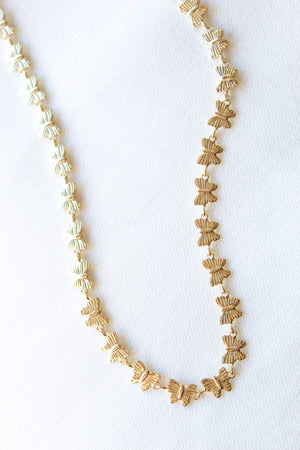 The Harper Necklace by Kinsey Designs Archives, a gold-filled butterfly-shaped piece, is displayed on a white textured fabric background.