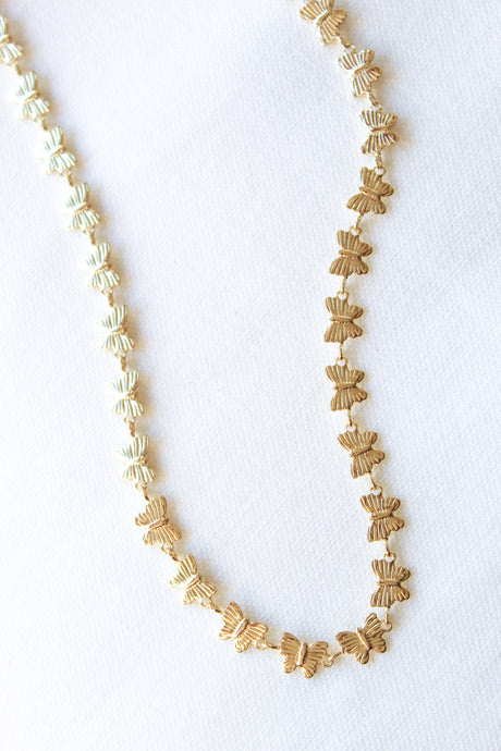 The Harper Necklace by Kinsey Designs Archives, a gold-filled butterfly-shaped piece, is displayed on a white textured fabric background.