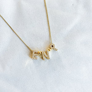 The Kinsey Designs Nurse Charm Necklace features sparkling gold-filled letter charms spelling “NURSE” on a white fabric background—a perfect necklace to showcase your dedication to the profession.