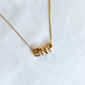 The Kinsey Designs Nurse Charm Necklace rests on a white fabric background, featuring a pendant that spells "NURSE"—the perfect profession necklace.