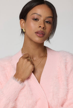 A woman in a pink fuzzy sweater wears gold filled jewelry and the Pozey Necklace by Kinsey Designs, gazing confidently against a plain backdrop. Perfect for our SAMPLE SALE.