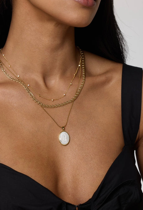 A woman wears a black top paired with the Kinsey Designs Archives Bailey Necklace, a 16" gold chain featuring an embossed pendant, styled with layered gold necklaces.