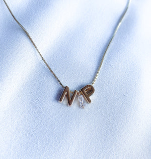The Kinsey NP Adjustable Necklace by Kinsey Designs features "N" and "P" letter charms with a small crystal, perfect as a profession necklace, and is displayed on white fabric.