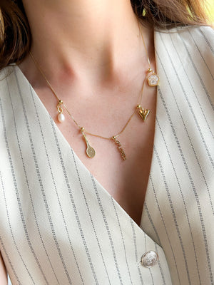 A close-up of the Kinsey Designs Florida Grip Charm, a vacation-ready piece, styled on a charm bar necklace and worn with a cream pinstripe vest.
