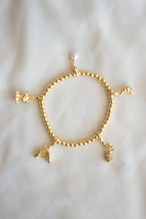 The Croissant Clip Charm by Kinsey Designs is featured on a gold filled beaded bracelet with four unique charm slides, shown on a soft, light-colored fabric background.