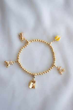 The Kinsey Designs Baby Bottle Clip Charm is styled on a gold filled beaded bracelet with four other unique charms from the Kinsey Charm Bar, displayed on a soft white fabric background.