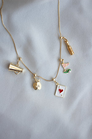 The Kinsey Designs Archives A+ Apple Grip Charm Bar Necklace, with fun charms like a megaphone, playing card, and bottle, makes a charming Teacher Appreciation Gift on light fabric.