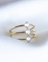 The Indy Ring by Kinsey Designs Archives features three round clear cubic zirconia stones set in a row on a gold filled band, shown against a white fabric background.