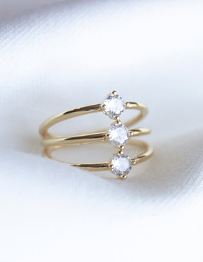 The Indy Ring by Kinsey Designs Archives features three round clear cubic zirconia stones set in a row on a gold filled band, shown against a white fabric background.